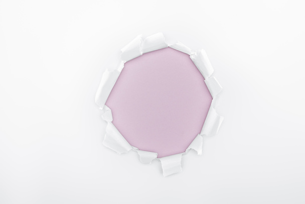 ragged hole in textured white paper on light purple background  - Foto, Imagen