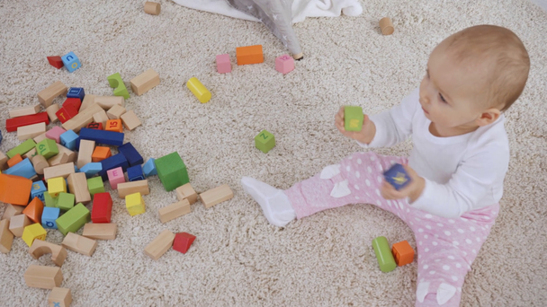 niño recogiendo bloques de madera mientras la hermana pequeña se sienta en la alfombra y juega con cubos
 - Imágenes, Vídeo