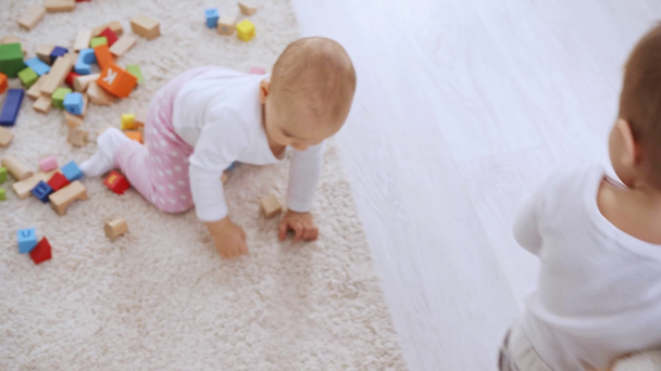 vista aerea del bambino che cammina con orsacchiotto mentre carina sorellina che gioca in moquette con cubi multicolori in legno
 - Filmati, video