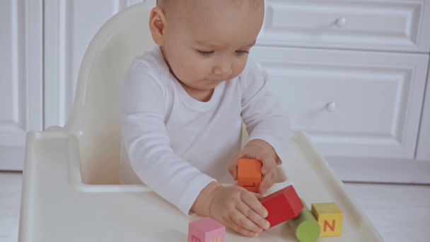 schattig kind zittend in de stoel, dan moeder geeft haar houten veelkleurige blokken en baby dropping Cube - Video
