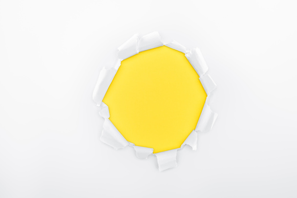torn hole in white textured paper on yellow background  - Foto, imagen
