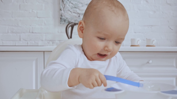 cute child sitting in highchair, then mother giving her spoon and bowl and baby playing with plastic dishes - Footage, Video