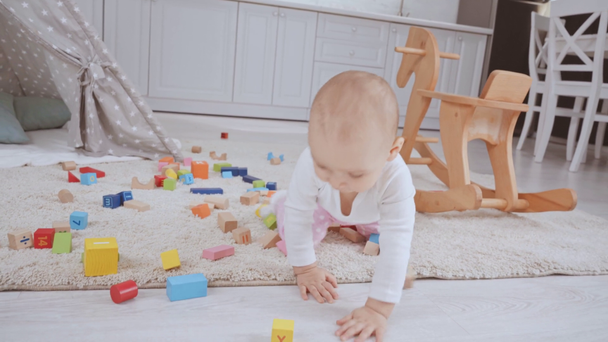 lindo niño arrastrándose a cuatro patas en la alfombra entre cubos multicolores de madera
 - Metraje, vídeo