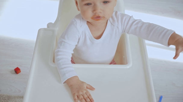 aranyos játékos gyermek geszturing ülve magasszékben a piszkos száj - Felvétel, videó