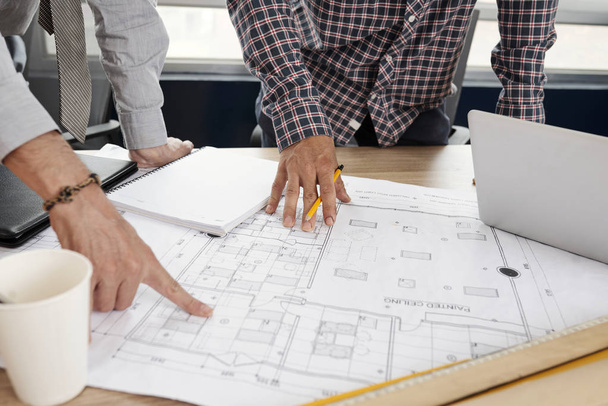 Команда инженеров-строителей обсуждает бумажный чертеж на офисном столе
 - Фото, изображение