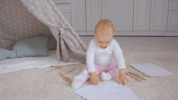 cute toddler kid sitting on fluffy carpet near baby wigwam and playing with papers and color pencils - Footage, Video