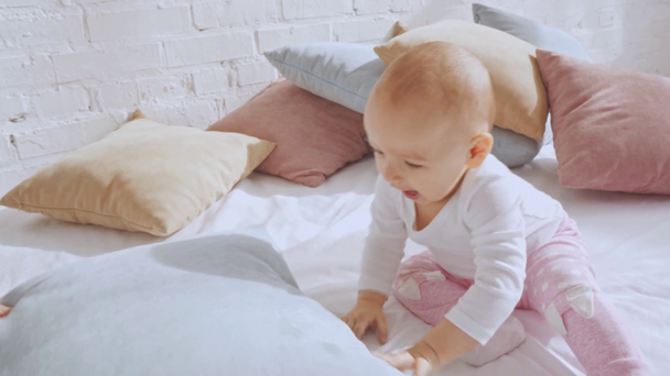 imádnivaló boldog tipegő gyermek ül az ágyban, és játszani párnák - Felvétel, videó