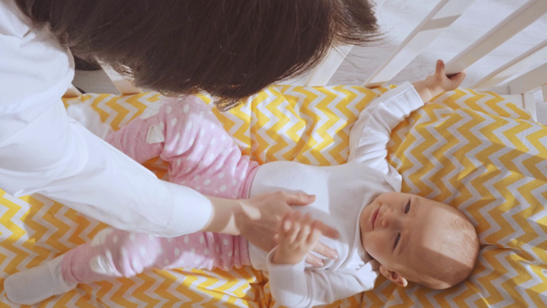 Blick von oben auf ein lächelndes Kind, das im Babybett liegt und dann von der Mutter gestreichelt wird - Filmmaterial, Video