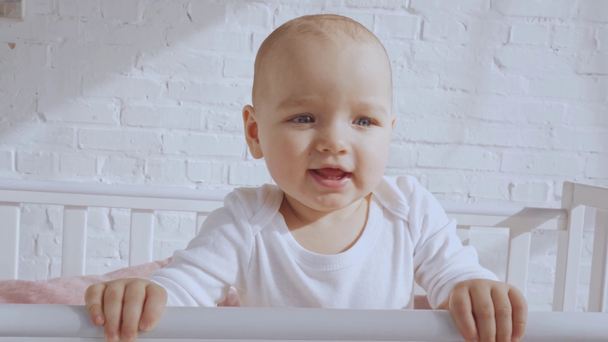 bebê adorável sorrindo e rindo no berço do bebê perto da parede de tijolo branco
 - Filmagem, Vídeo