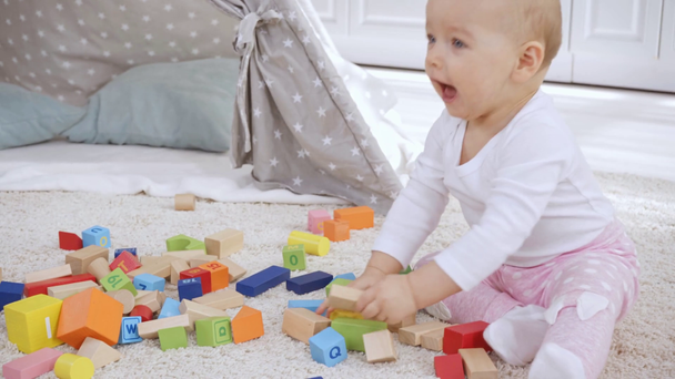 sevimli Toddler çocuk halı üzerinde çok renkli ahşap bloklar ile oynuyor  - Video, Çekim