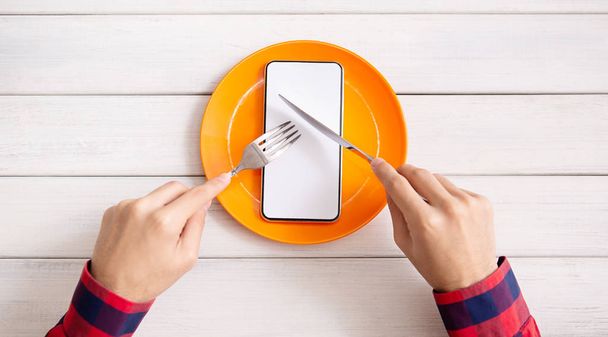 Man eating blank smartphone with knife and fork - Foto, immagini