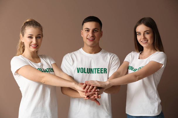 Team of young volunteers putting hands together on color background - Photo, Image