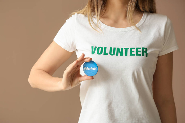 Young female volunteer with badge on color background - Foto, imagen