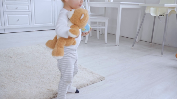cute chłopiec maluch działa z misia w mieszkaniu, a następnie grając z piłką na dywan - Materiał filmowy, wideo
