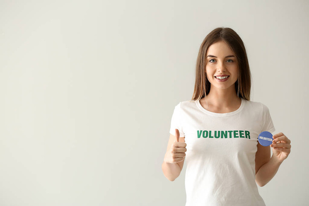 Jonge vrouwelijke vrijwilliger met badge op lichte achtergrond - Foto, afbeelding