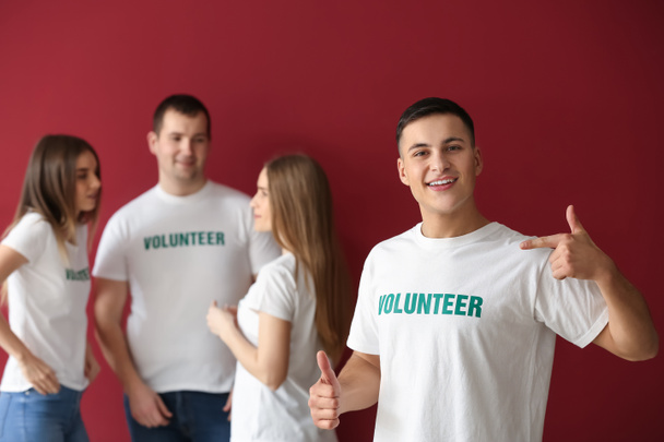 Young male volunteer and his team on color background - Photo, Image