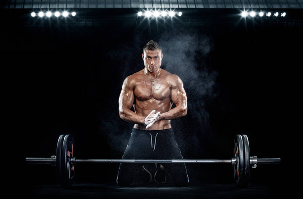 Photo of strong muscular bodybuilder athletic man pumping up muscles with barbell on black background. Workout energy bodybuilding concept. - Фото, зображення