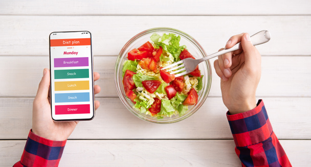 Homem usando smartphone com menu diário e comer salada
 - Foto, Imagem