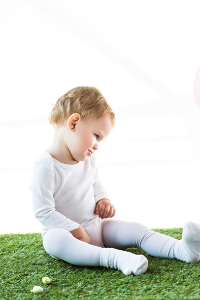 adorable blonde child sitting on green grass isolated on white - Foto, Bild