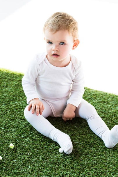 adorable blonde baby sitting on green grass isolated on white - Фото, изображение