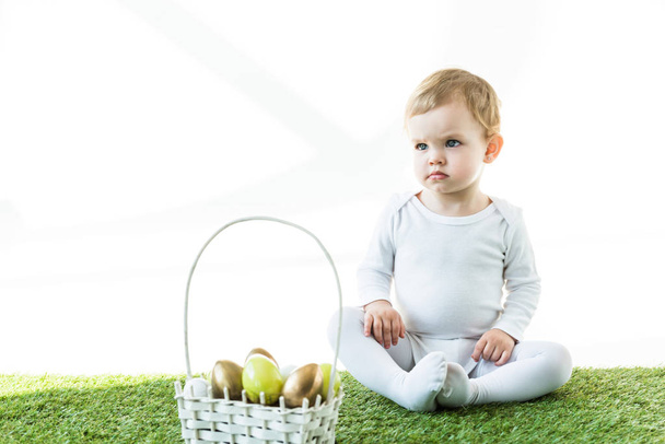 mignon bébé assis sur l'herbe verte près panier de paille avec des œufs colorés de l'Est isolé sur blanc
 - Photo, image