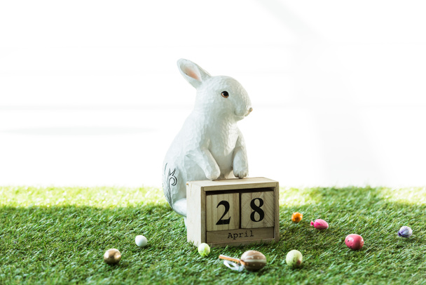 decorative rabbit, wooden calendar with 28 April date, and colorful Easter eggs on green grass   isolated on white - Fotoğraf, Görsel