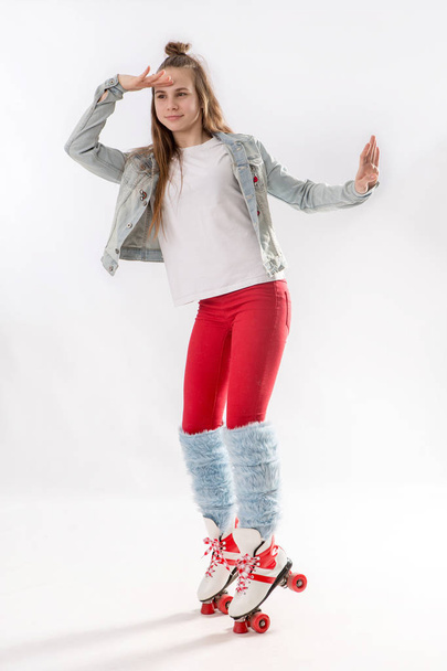 Young beautiful girl in sporty stylish clothes with long hair on four-wheeled rollers isolated on background - Zdjęcie, obraz