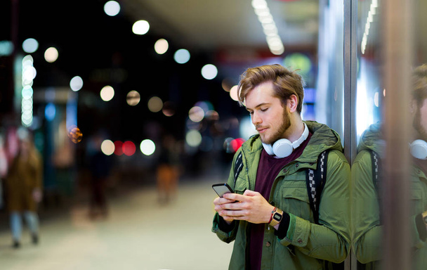 Νεαρός άνδρας χρησιμοποιώντας smartphone σε αστικό δρόμο τη νύχτα - Φωτογραφία, εικόνα