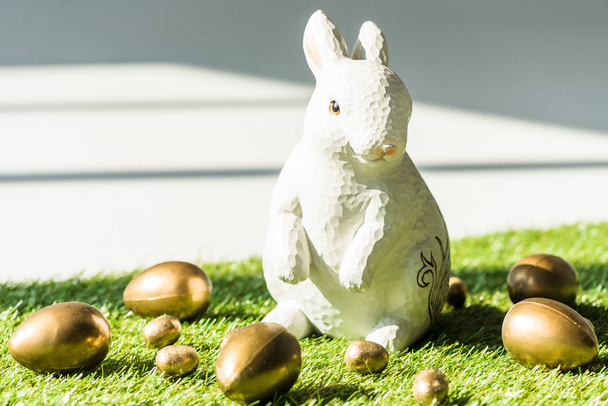 decorative Easter rabbit end shiny golden eggs on green grass surface - Фото, изображение