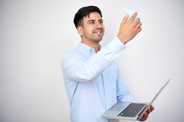 Θετική νεαρός άνδρας με το laptop λήψη selfie ή γυρίσματα βίντεο για κανάλι σχετικά με τις νέες συσκευές - Φωτογραφία, εικόνα