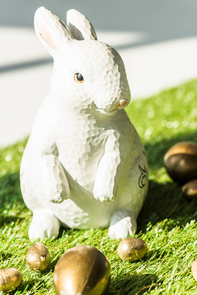 selective focus of decorative Easter rabbit end shiny Easter eggs on green grass surface - Fotó, kép