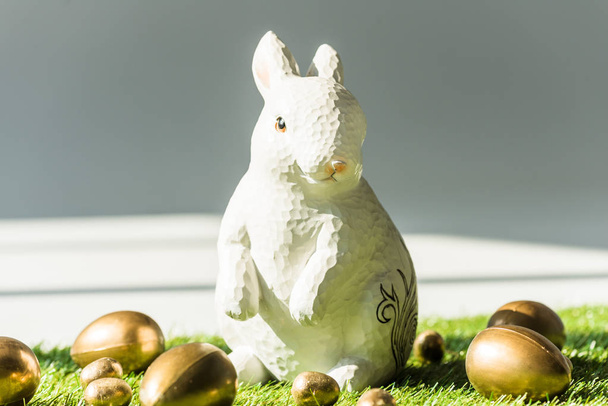 Easter rabbit end shiny golden Easter eggs on green grass surface - Фото, изображение