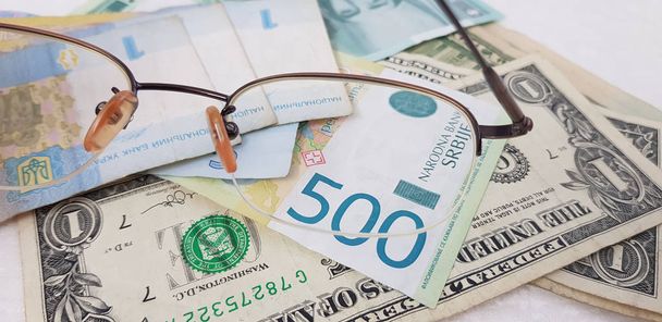 banconote di dinari grivna e dollari viste attraverso occhiali da vista su tavolo bianco
 - Foto, immagini