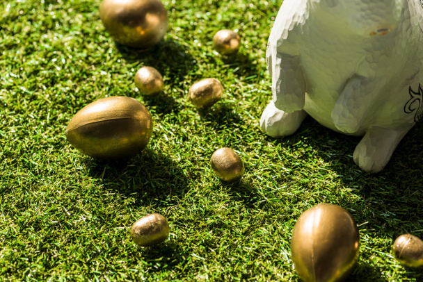 golden Easter eggs and decorative rabbit on green grass surface - Fotó, kép