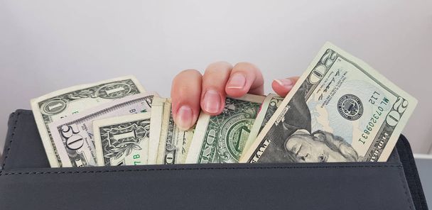 dedos femininos em um grupo de notas de dólar americano em um bolso de pasta de couro preto
 - Foto, Imagem