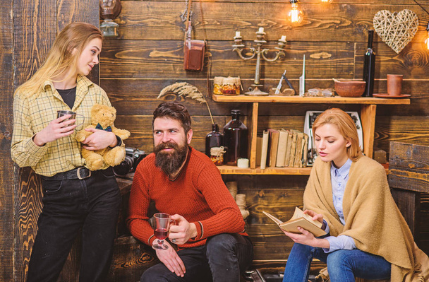 Woman wrapped in woolen blanket reading book. Cheerful bearded man in retro outfit drinking mulled wine while talking to his daughter. Teenage girl spending time with parents, happy family concept - Foto, Imagem