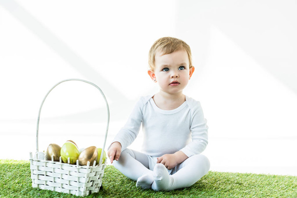 cute baby sitting near straw basket with Easter eggs isolated isolated on white - Foto, Bild
