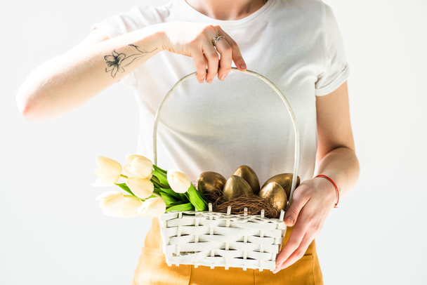 vista parziale di donna che tiene cesto di paglia bianca con uova di Pasqua e tulipani isolati su bianco
 - Foto, immagini