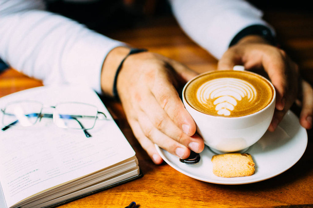 De hand van een man zittend aan een tafel met een kopje aromatische koffie, een telefoon en een notebook. Zakenlunch - Foto, afbeelding