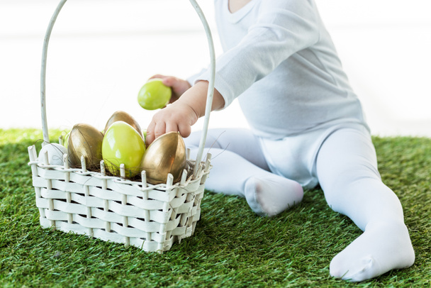 partial view of baby taking colorful Easter eggs from straw basket isolated on white - Foto, immagini