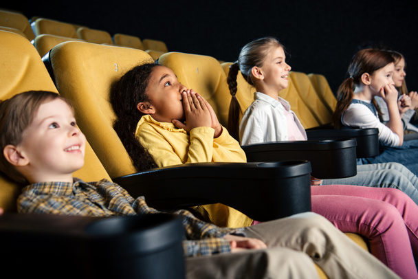 sonrientes amigos multiculturales sentados en el cine y viendo películas juntos
 - Foto, imagen