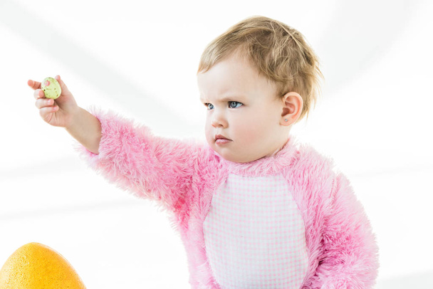 чарівна дитина тримає барвисте перепелине яйце в простягнутій руці ізольовано на білому
 - Фото, зображення