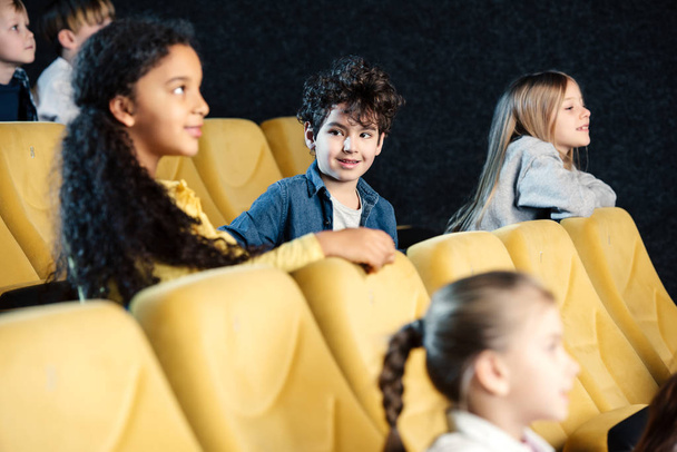 selective focus of multicultural kids sitting in cinema and watching movie - Photo, image