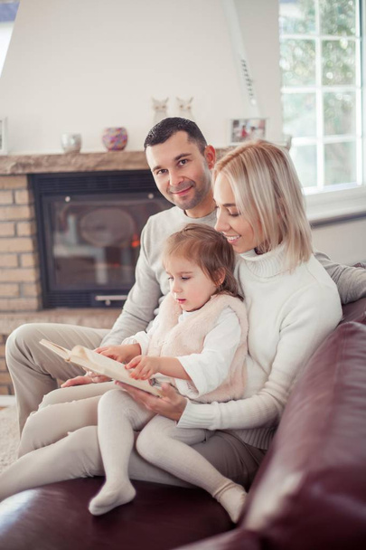 Beautiful young family is reading a book near the fireplace. Cozy. - Photo, Image