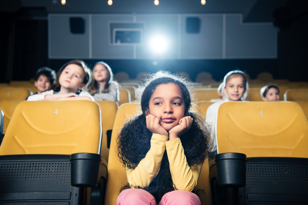 pensive african american child sitting in cinema together with friends - Foto, Imagem