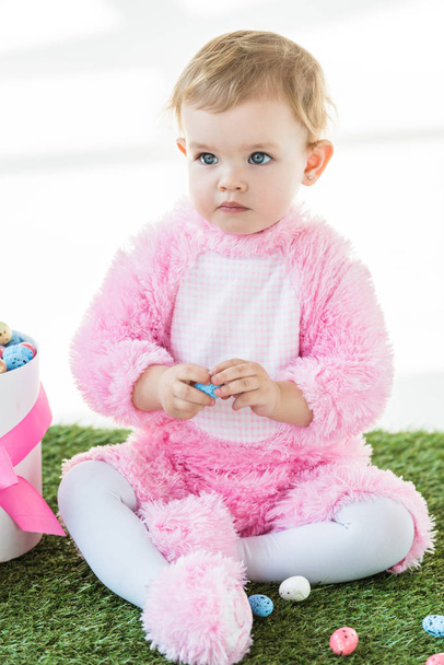 cute dreamy kid in pink fluffy costume sitting near box with Easter eggs isolated on white - Foto, Imagem