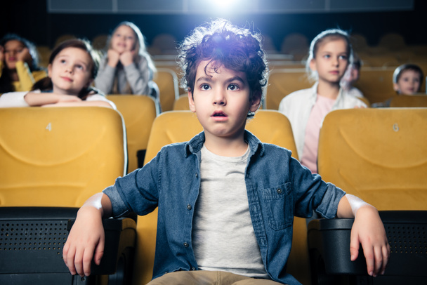 concentrated mixed race boy watching movie in cinema together with multicultural friends - Photo, Image