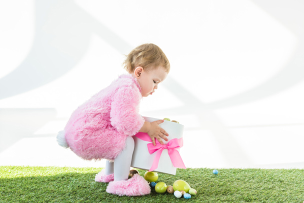 adorable niño en rosa esponjoso traje caja de espera con arco rosa y coloridos huevos de Pascua aislados en blanco
 - Foto, Imagen