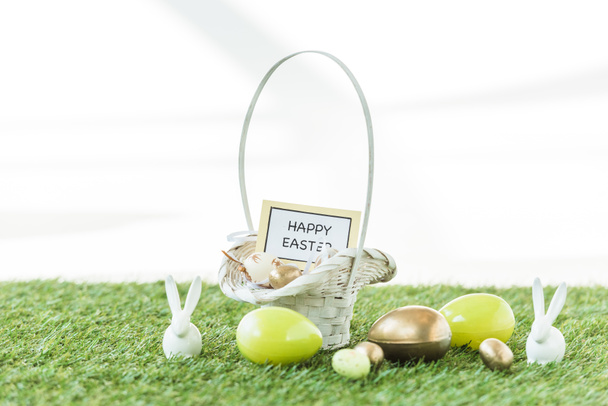 ovos de Páscoa coloridos, coelhos decorativos e cesta de palha com cartão de Páscoa feliz isolado no branco
 - Foto, Imagem