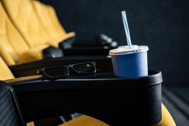 селективное фокусирование пустых оранжевых сидений кинотеатра с чашкой для утилизации и 3D очками
 - Фото, изображение